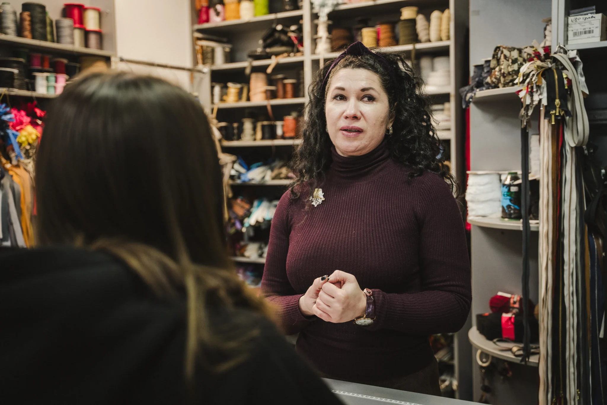 Продавчиня Наталі Ветіганцева розповідає історію крамниці. на ній - пурпуровий гольф з брошкою.