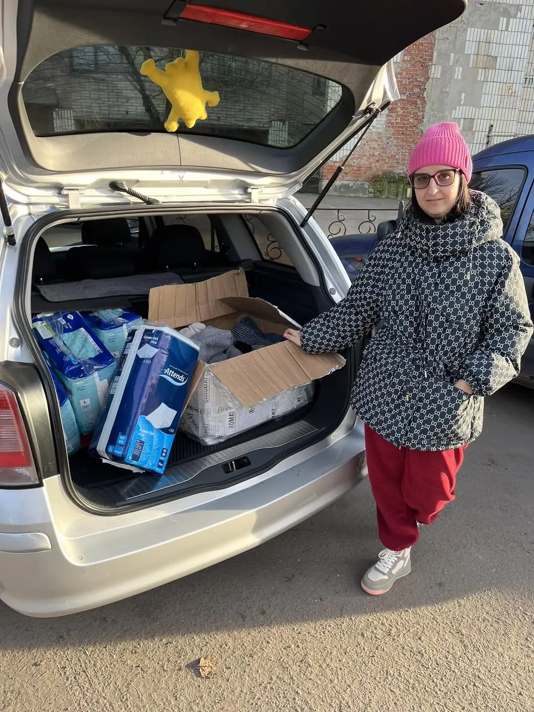 Жінка стоїть біля багажнику машини