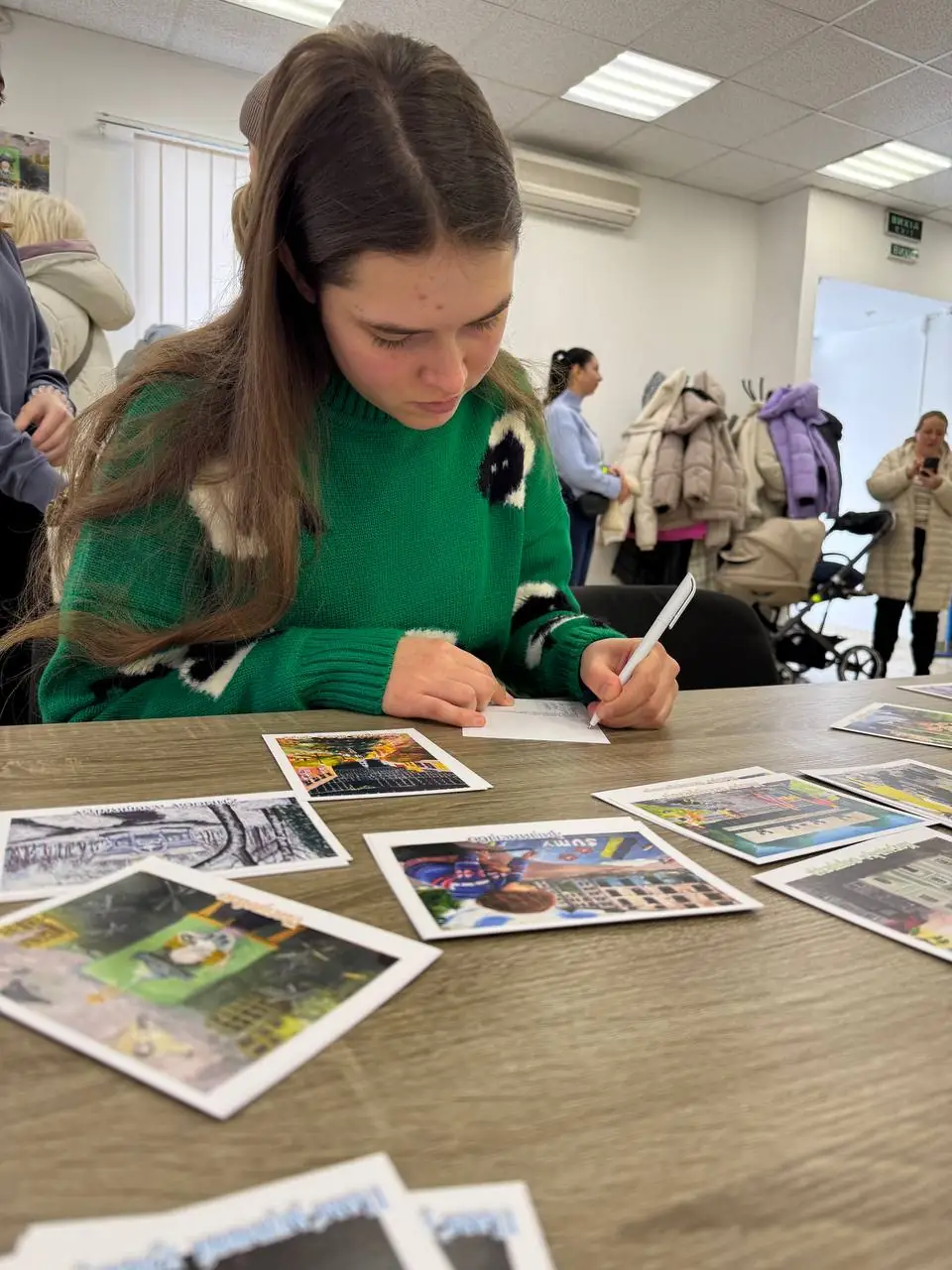 Дівчина підписує листівку з дитячим малюнком для військових у Сумах