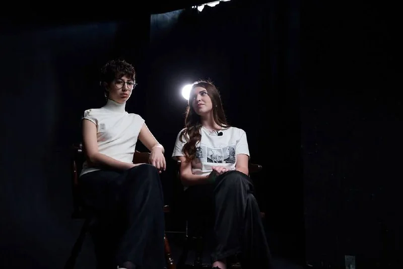 Дві дівчини у фільмі сидять на стільцях поруч.