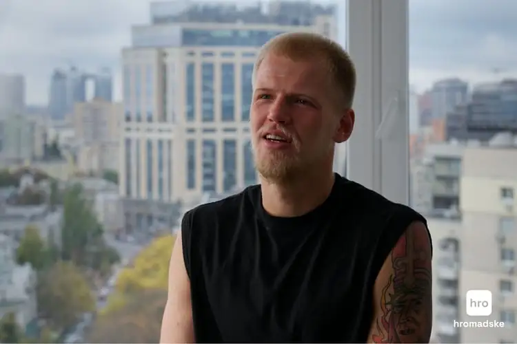 Військовий Дмитро Расті у чорній майці дає інтерв'ю. Позаду - скляні київські будинки.