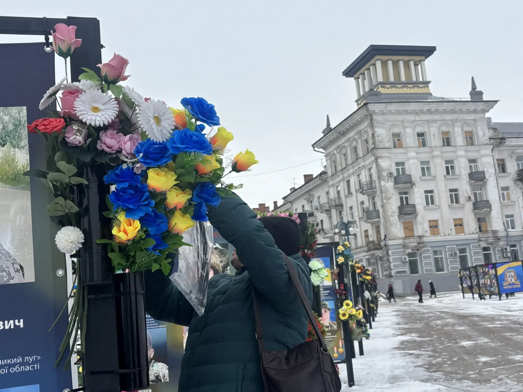 Жінка ремонтує пам'ятник у центрі міста. На ньому синьо-жовті квіти.