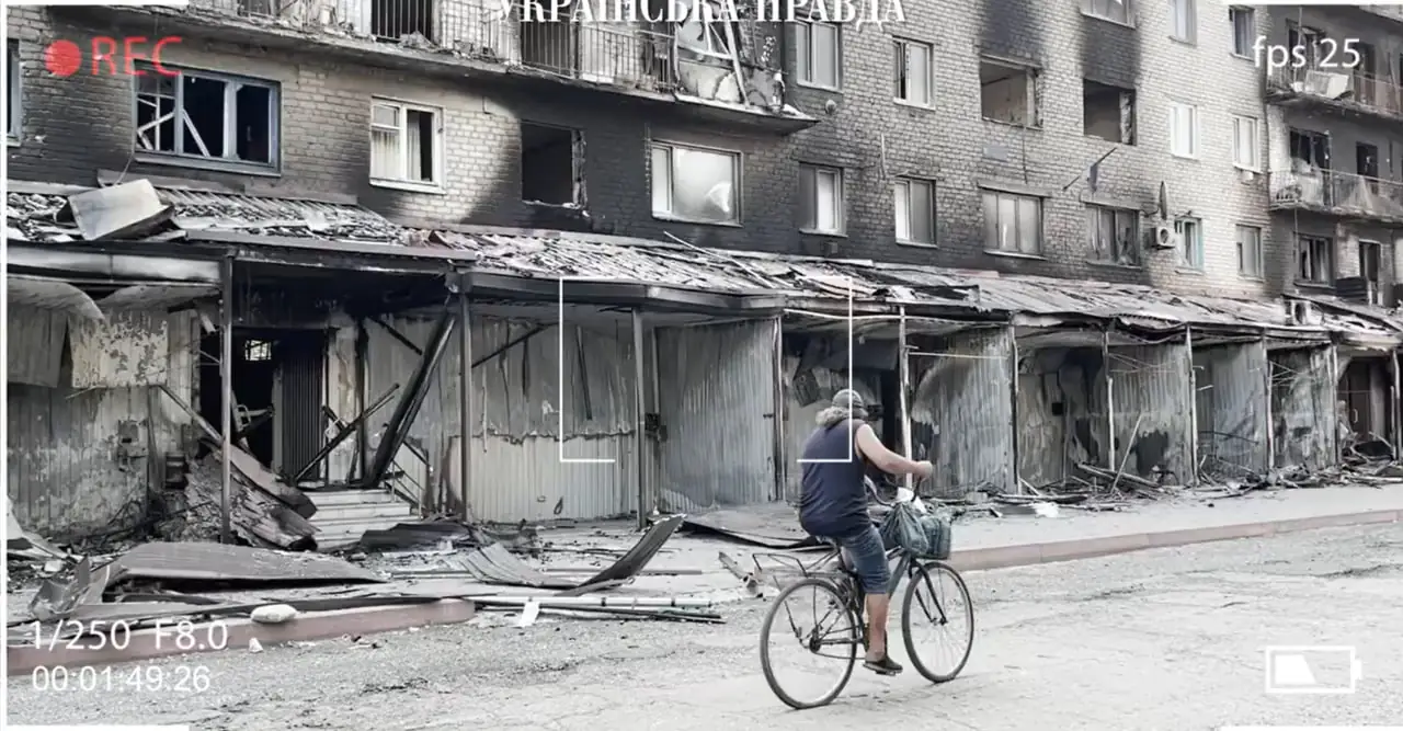 Чоловік на велосипеді проїжджає повз зруйнований будинок.