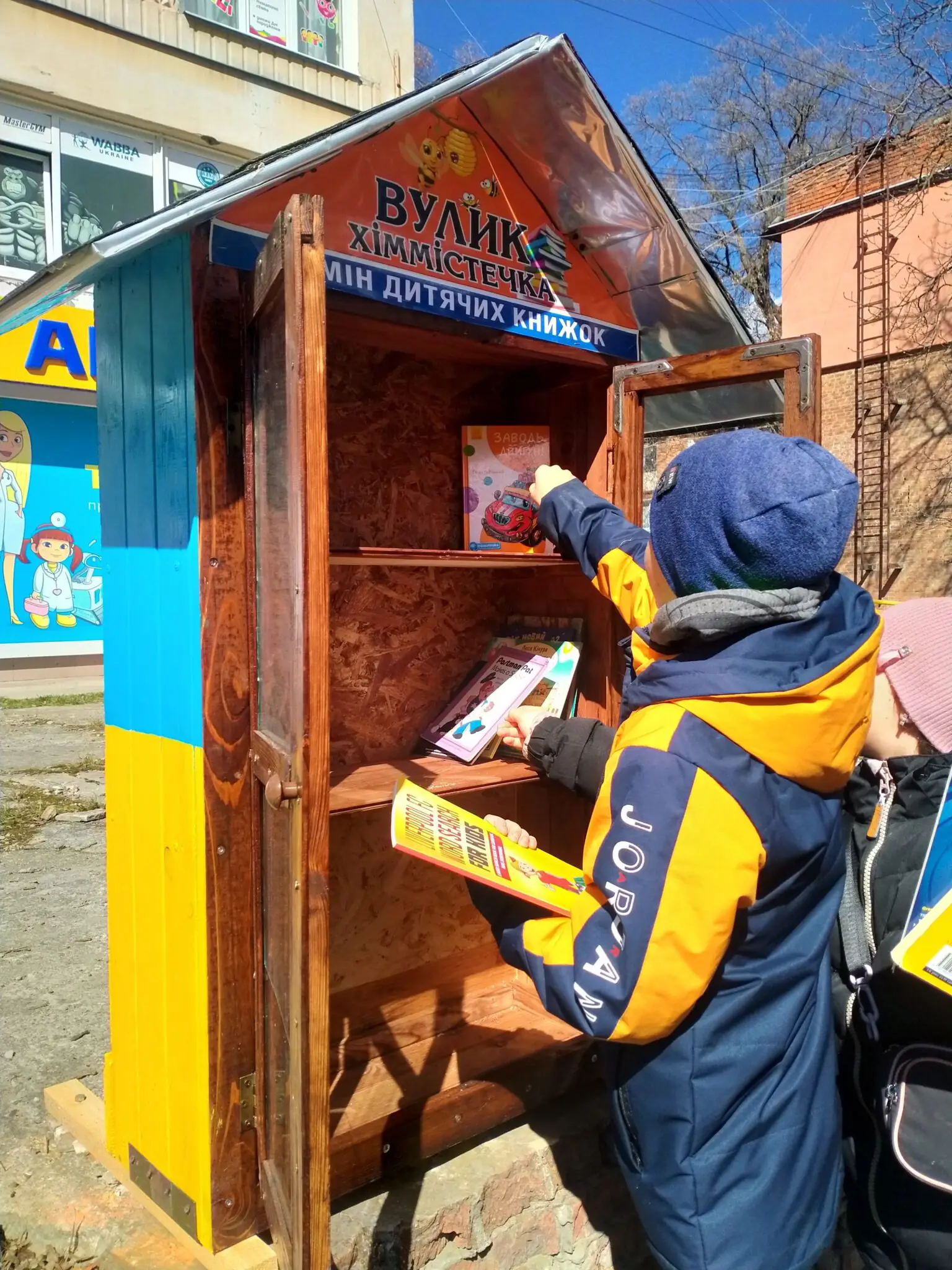 Хлопчик кладе книгу в мінібібліотеку